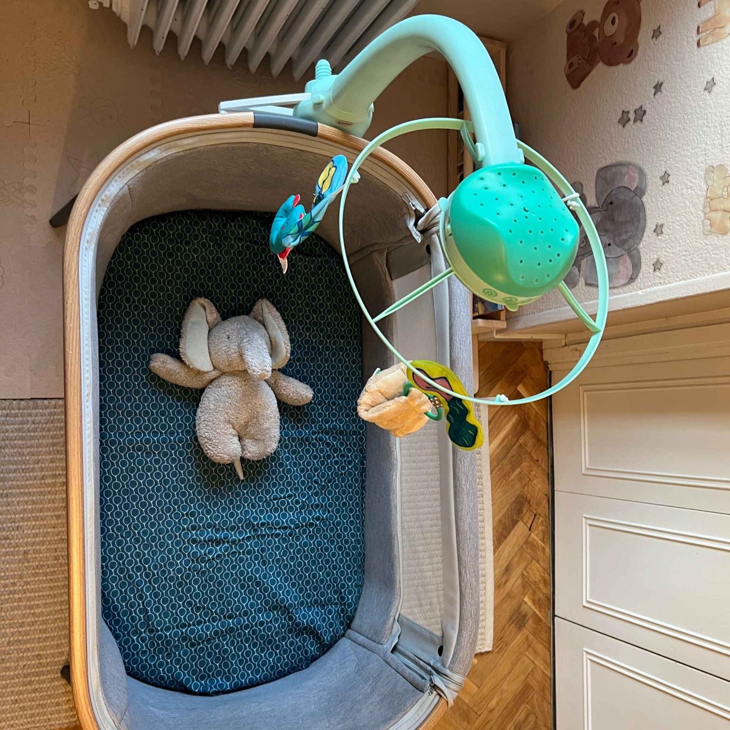 Maxi-cosi_Iora white CribClamp attached to the bedside crib with a little Infantino 3 in 1 musical mobile. View of the Maxi-cosi co-sleeper and baby mobile attachment adapter bracket from the above the bedside cot